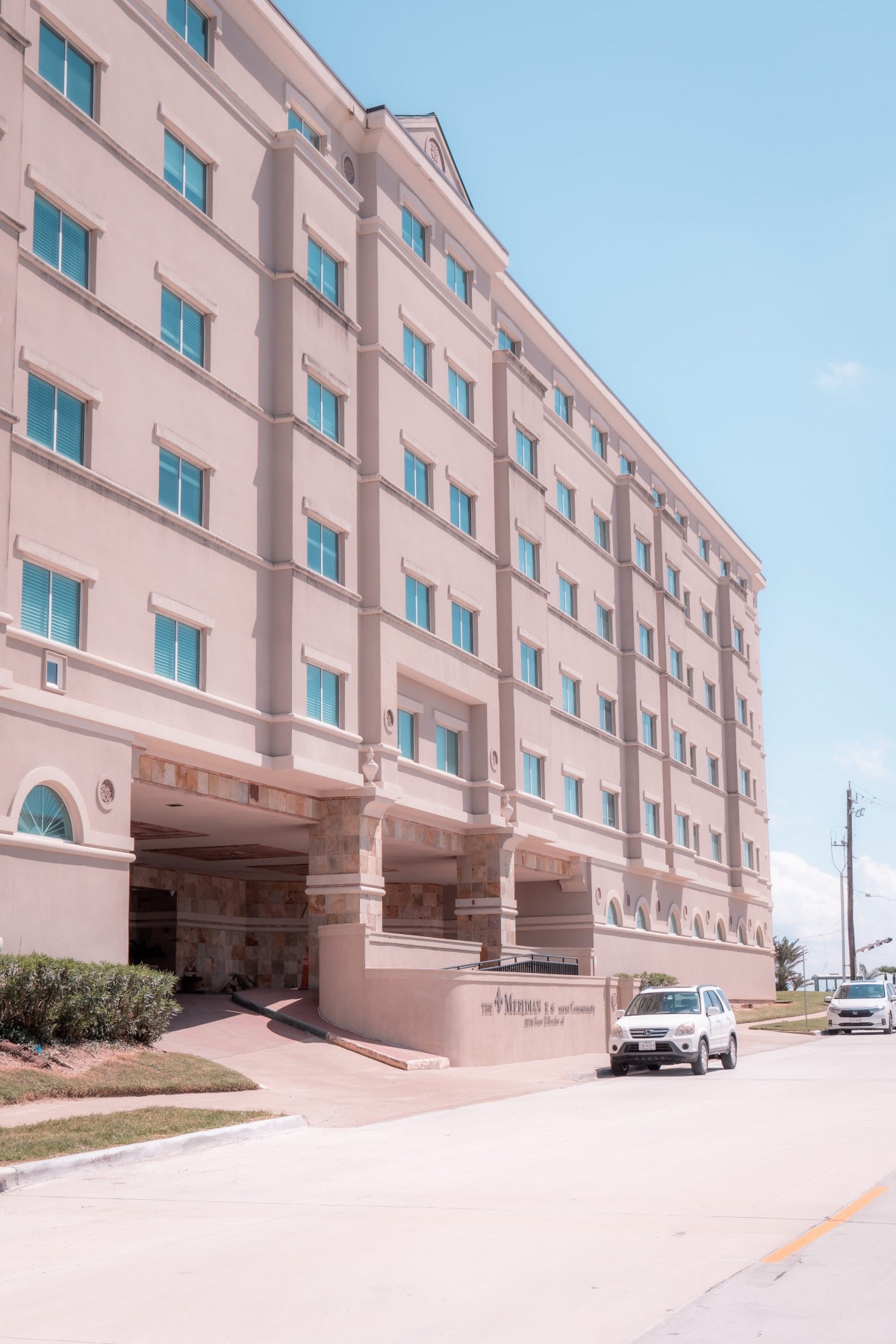 A multi-story hotel building with vehicles parked in front on a sunny day.
