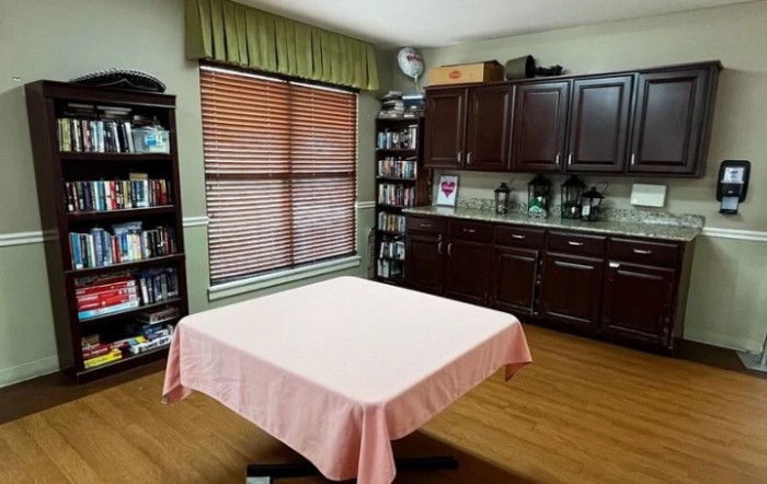A home interior with a table, bookshelves, and cabinets near a window.
