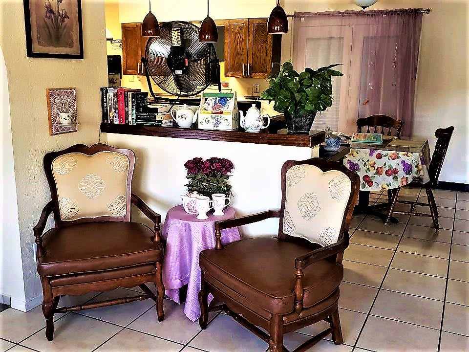 Cozy living room area with two armchairs and a small table adorned with flowers, surrounded by warm decor and indoor plants.