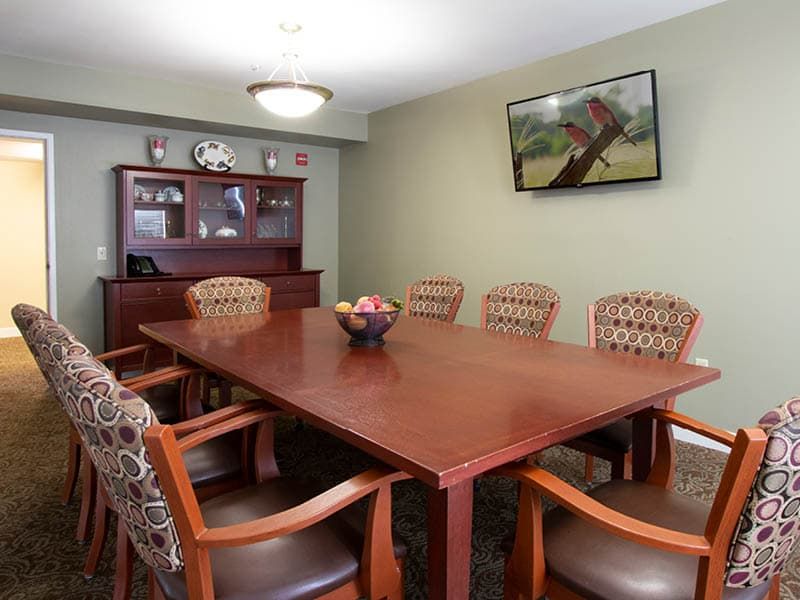 A well-furnished conference room featuring a large wooden meeting table surrounded by chairs, with a cabinet and decorative painting on the walls.