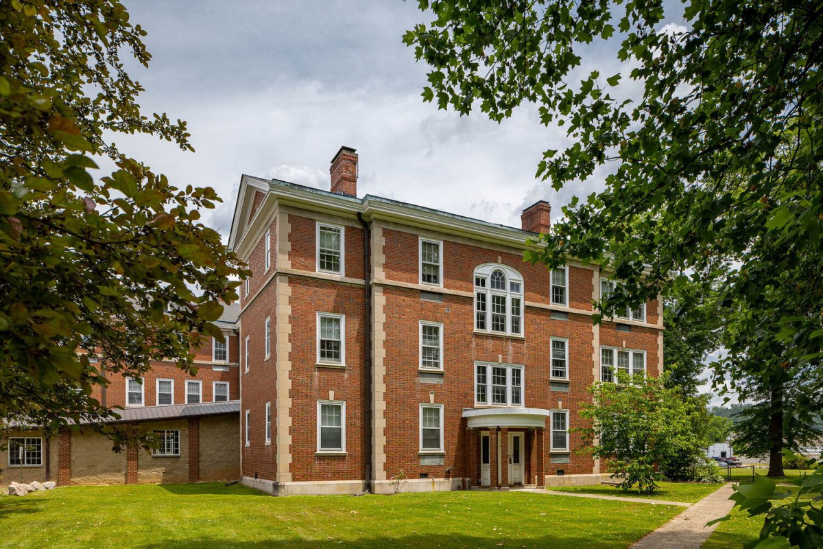 A historic brick building surrounded by trees under a cloudy sky.