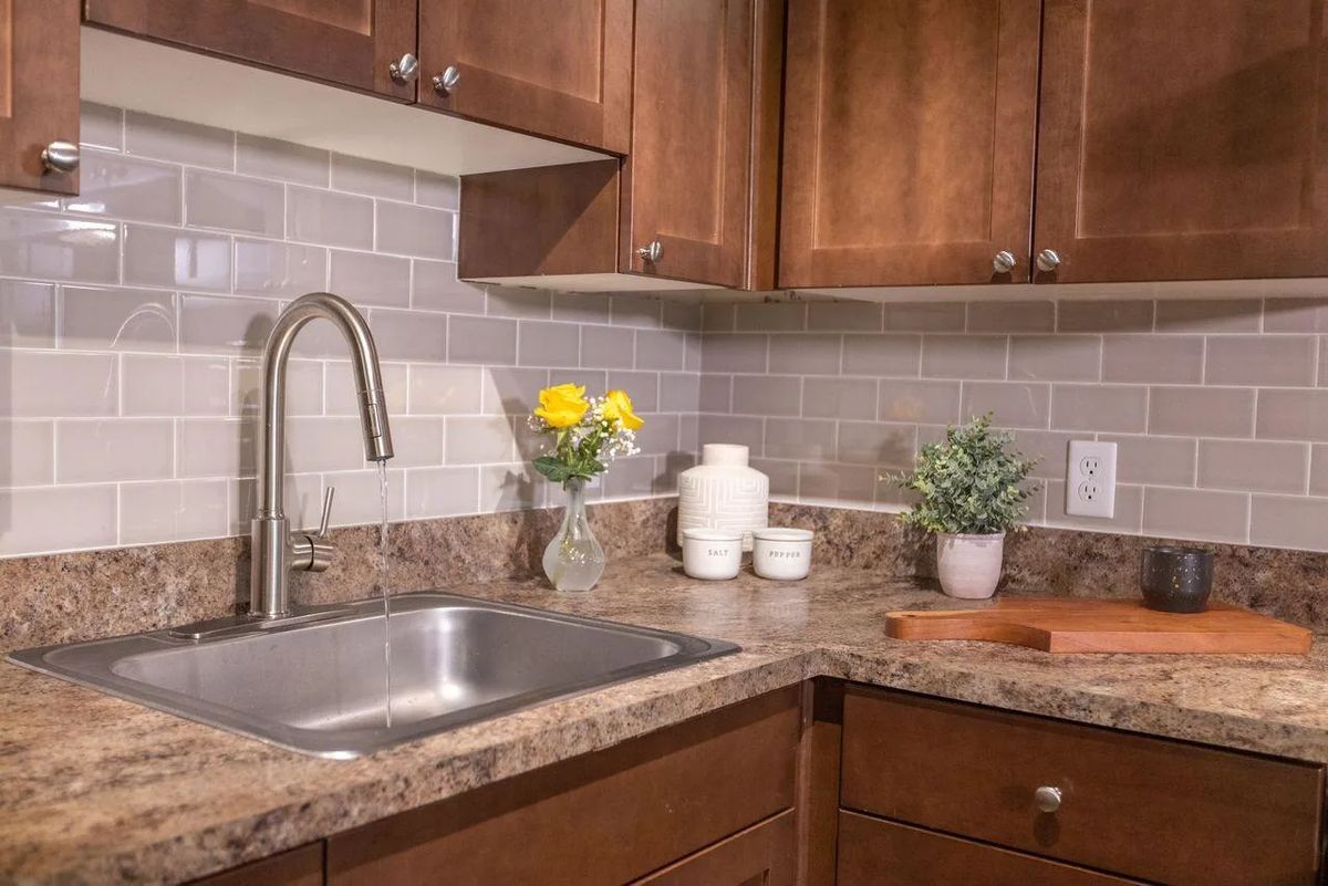 A tidy kitchen corner featuring a stainless steel sink, wooden cabinets, and decorative elements like flowers and jars.