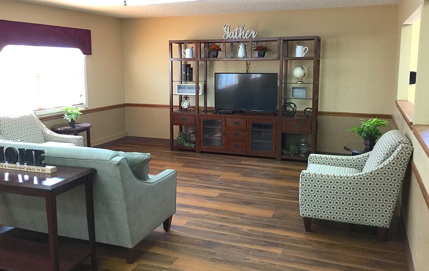 A cozy living room with a TV and comfortable seating arrangement, featuring wood flooring and decorative shelves.