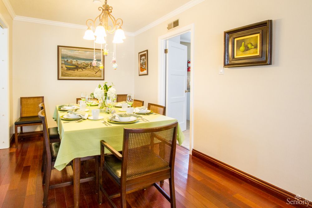 A cozy dining room with a neatly set table ready for a meal, featuring wooden chairs and elegant artwork on the walls.