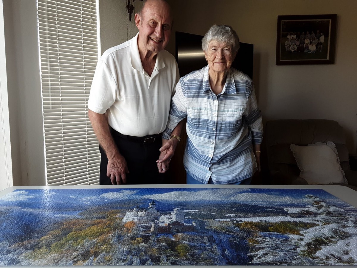 An elderly couple smiling and posing with a painting indoors.