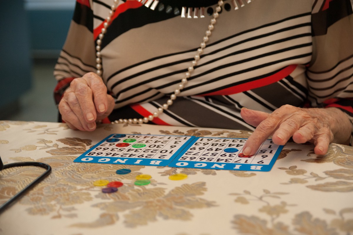 An elderly person playing bingo at a table with bingo cards and markers.