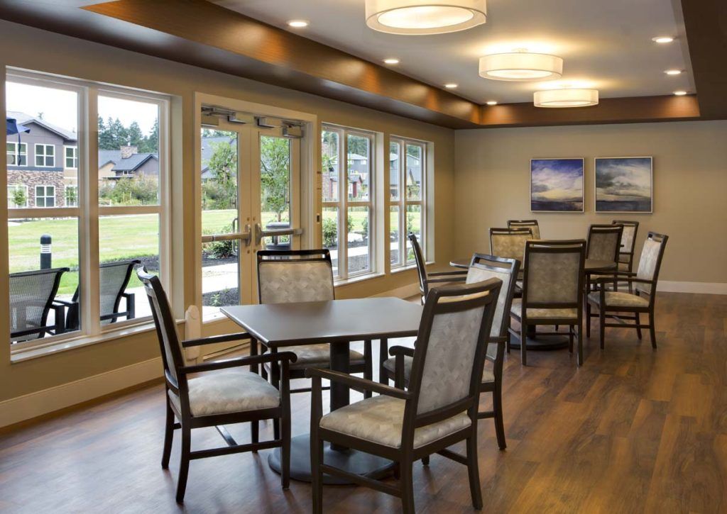 A well-lit dining room with wooden flooring and large windows overlooking a garden.
