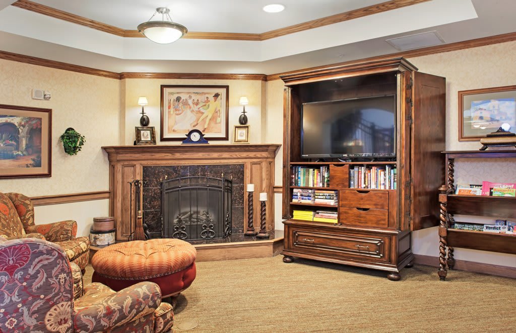 A cozy living room with a fireplace and a television set on a wooden bookshelf.
