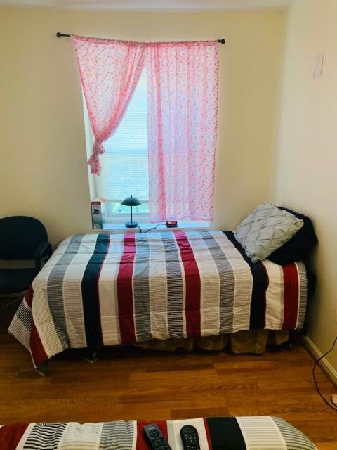 A cozy bedroom with a neatly made bed featuring a striped blanket, next to a window with pink curtains.