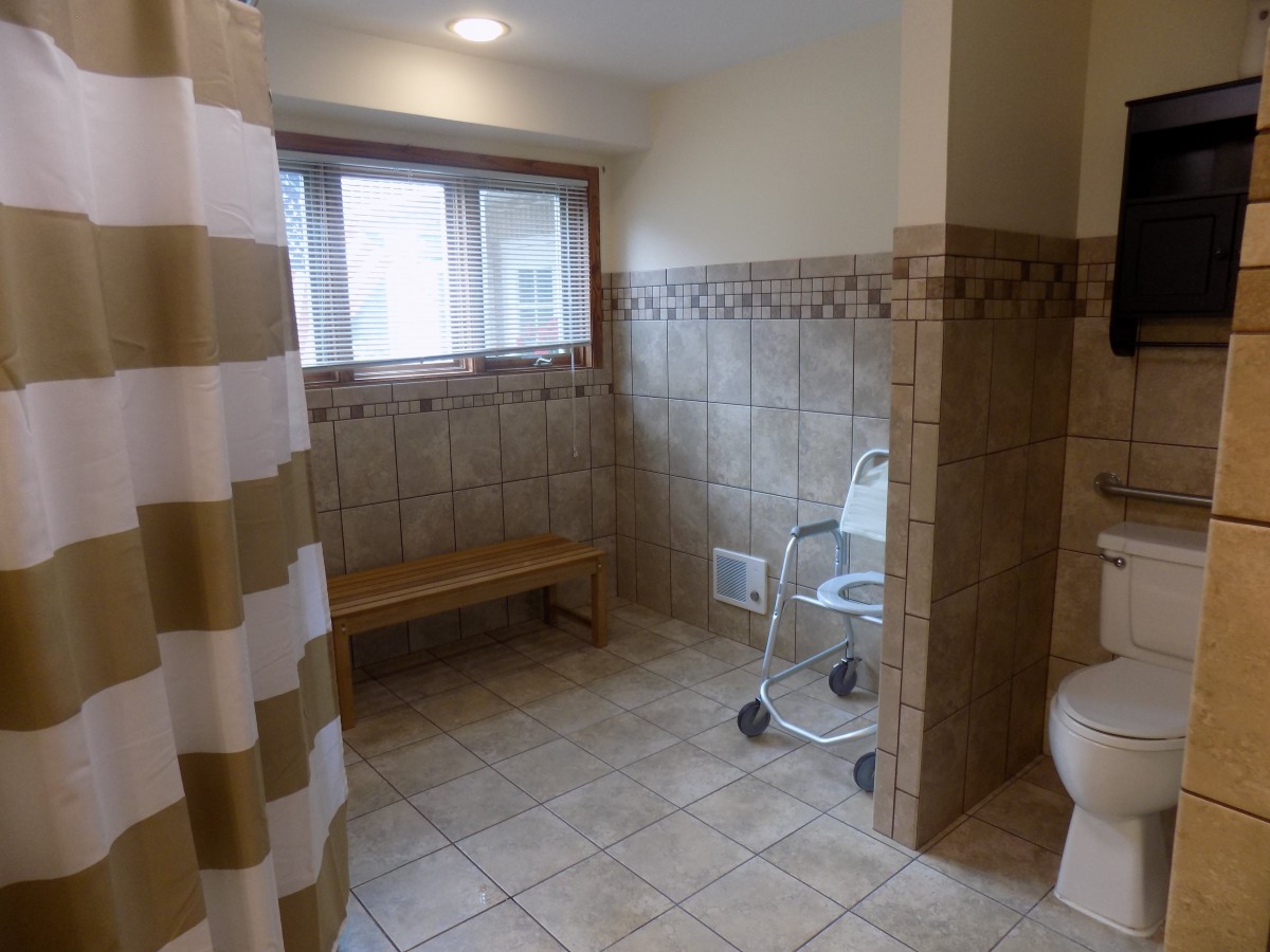 An accessible bathroom featuring tiled walls, a shower with a curtain, and a shower chair.