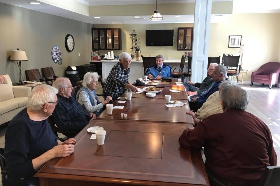 A group of seniors engaged in a discussion around a table in a community room.