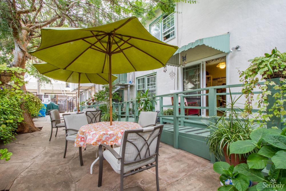 A cozy outdoor patio area with tables and umbrellas, surrounded by greenery.