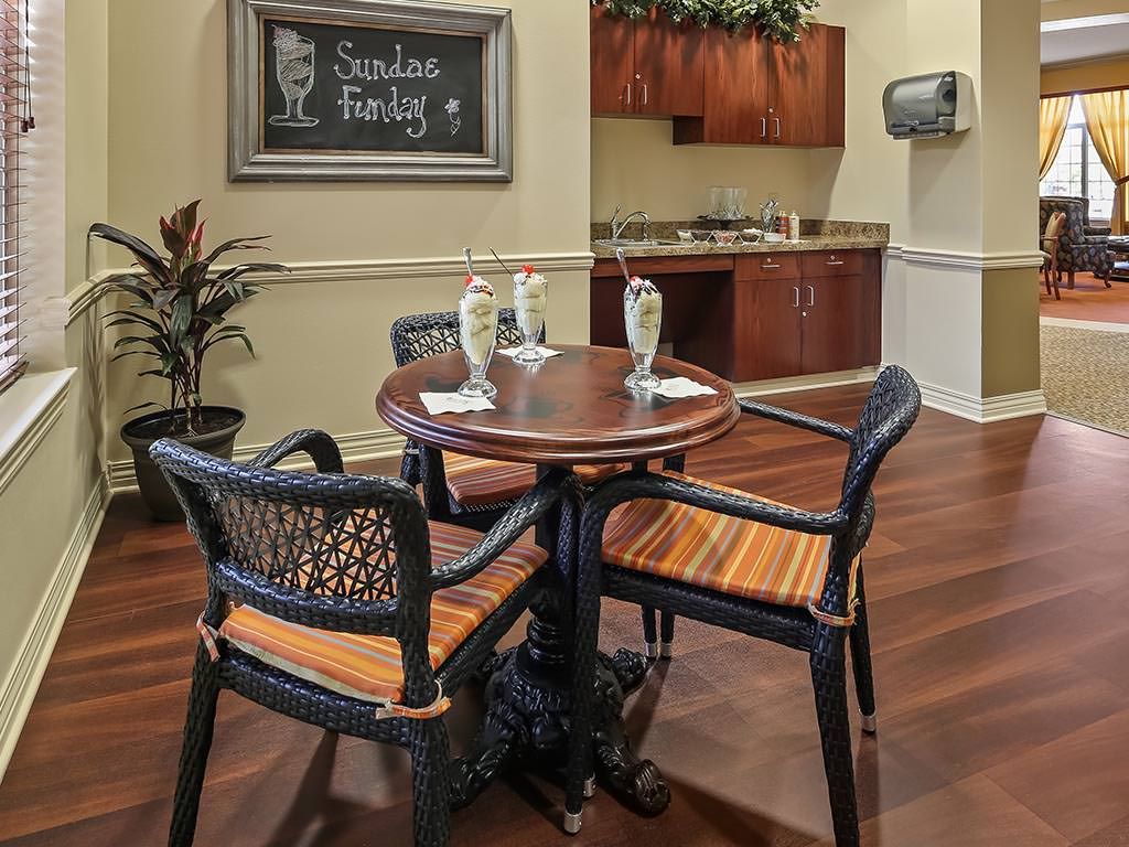 A cozy dining area with a round table and four chairs, featuring a chalkboard and kitchenette in the background.