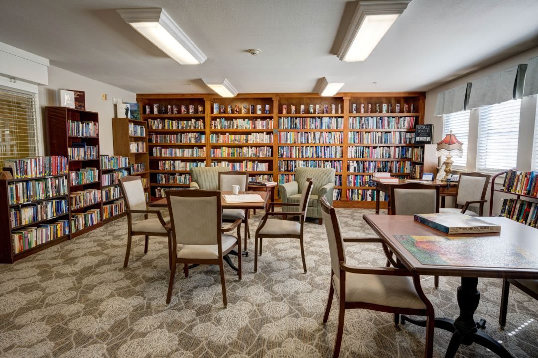 A cozy library reading area with bookshelves, tables, and chairs.