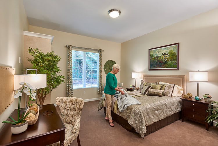 A woman making the bed in a well-decorated bedroom with various furniture and decor elements.