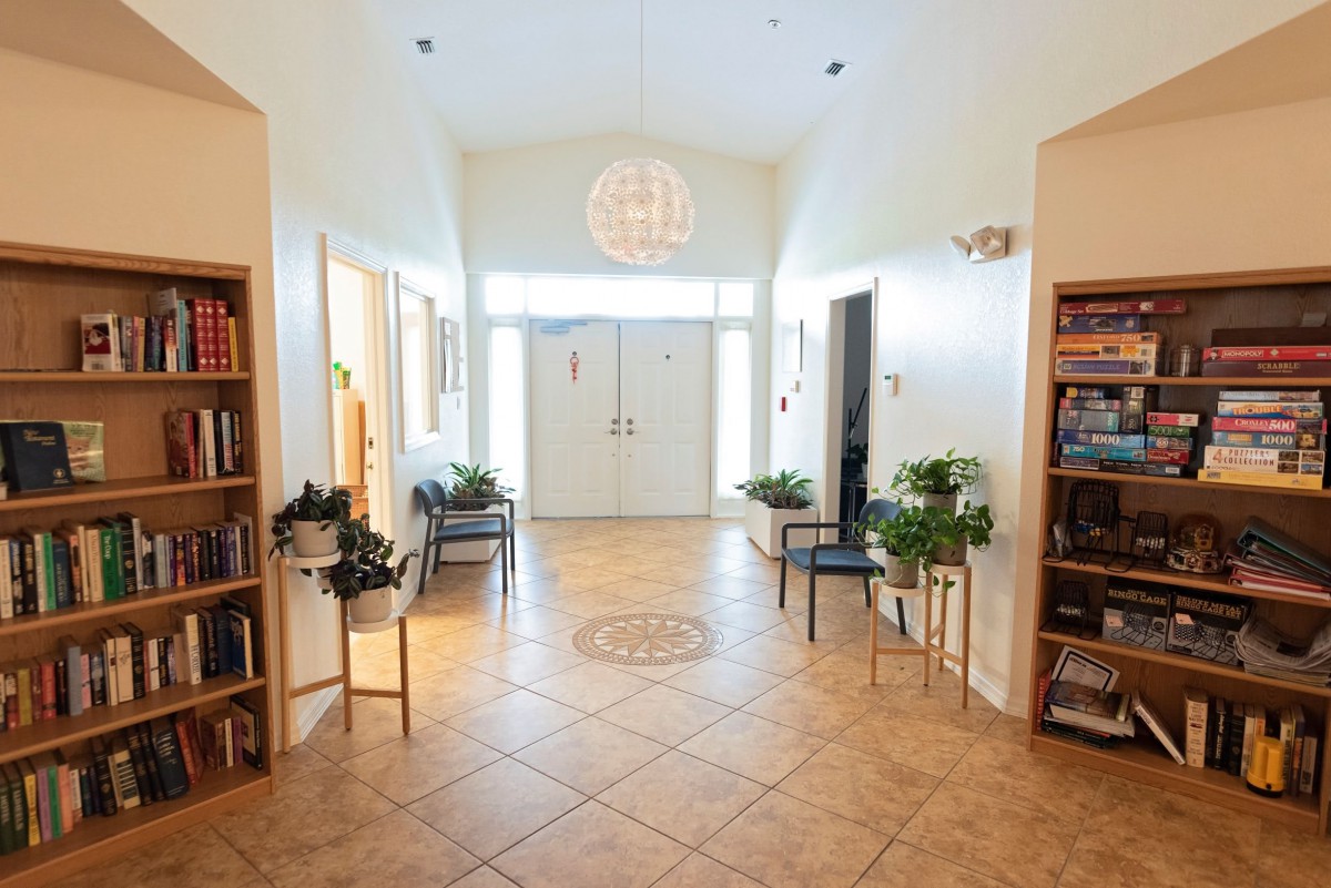 A bright hallway with tile flooring, plants, bookshelves, and chairs leading to a set of double doors.