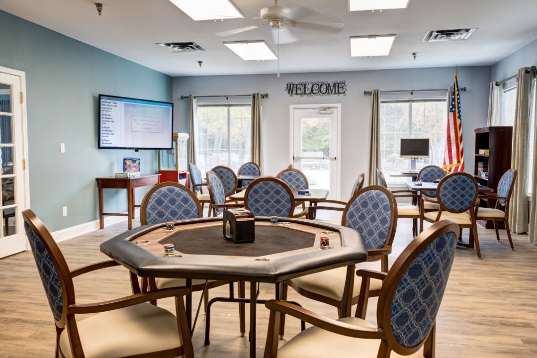 A well-furnished game room featuring multiple tables and comfortable seating, with a large screen on the wall.