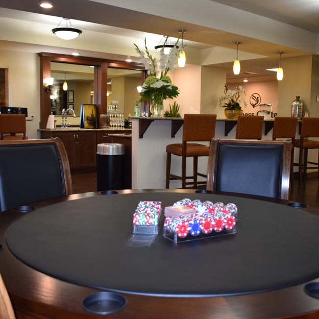 A modern room featuring a poker table with chips and a bar area in the background.