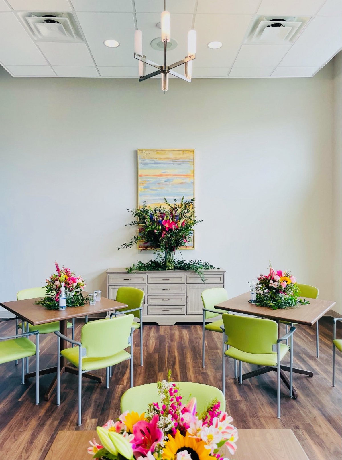 A modern dining area with green chairs, elegant flower arrangements, and wood flooring.