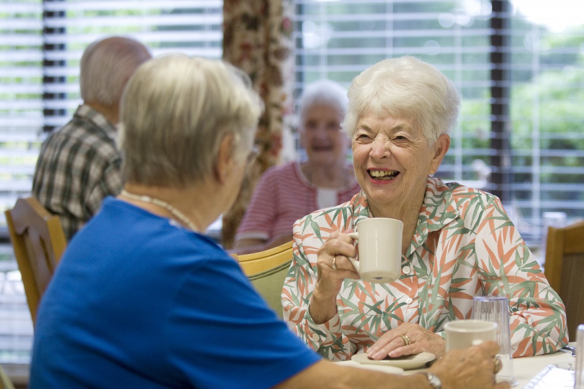 Elderly women enjoying a conversation over coffee in a communal setting.