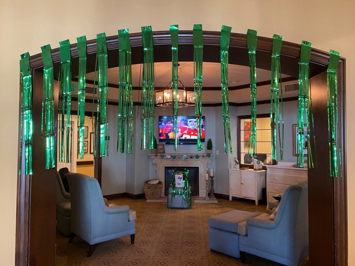 A cozy living room adorned with vibrant green streamers, featuring a television and fireplace surrounded by comfortable seating.