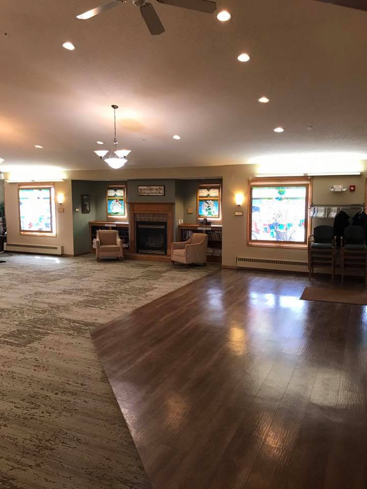 A spacious living room with a mix of carpet and hardwood flooring, featuring comfortable seating, large windows, and a fireplace.