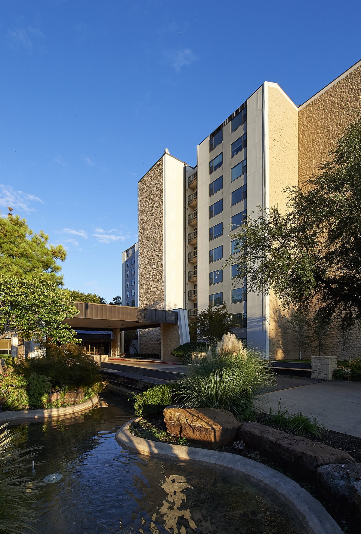 A view of a modern hotel building surrounded by landscaped greenery under a clear sky.