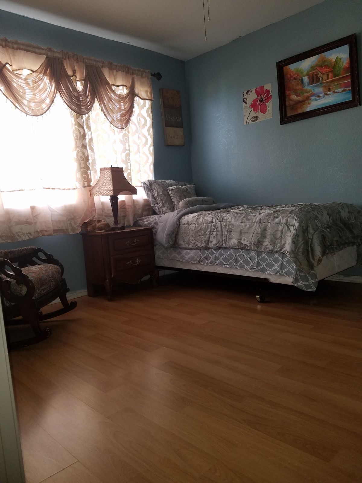 A cozy bedroom with a single bed, a nightstand with a lamp, and a rocking chair by the window.