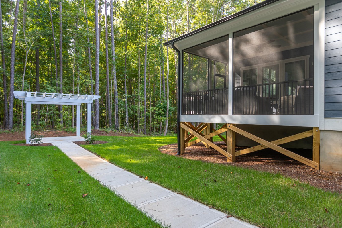 A serene backyard featuring a screened porch, pergola, and a pathway leading into lush greenery.