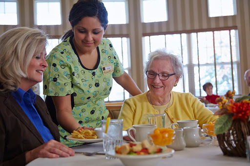 A caregiver serves a meal to elderly residents in a warm and inviting dining area.
