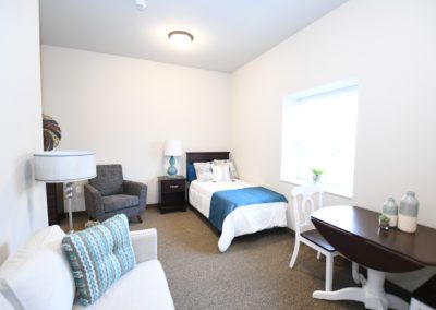 A cozy bedroom with a single bed, chair, lamp, and window.