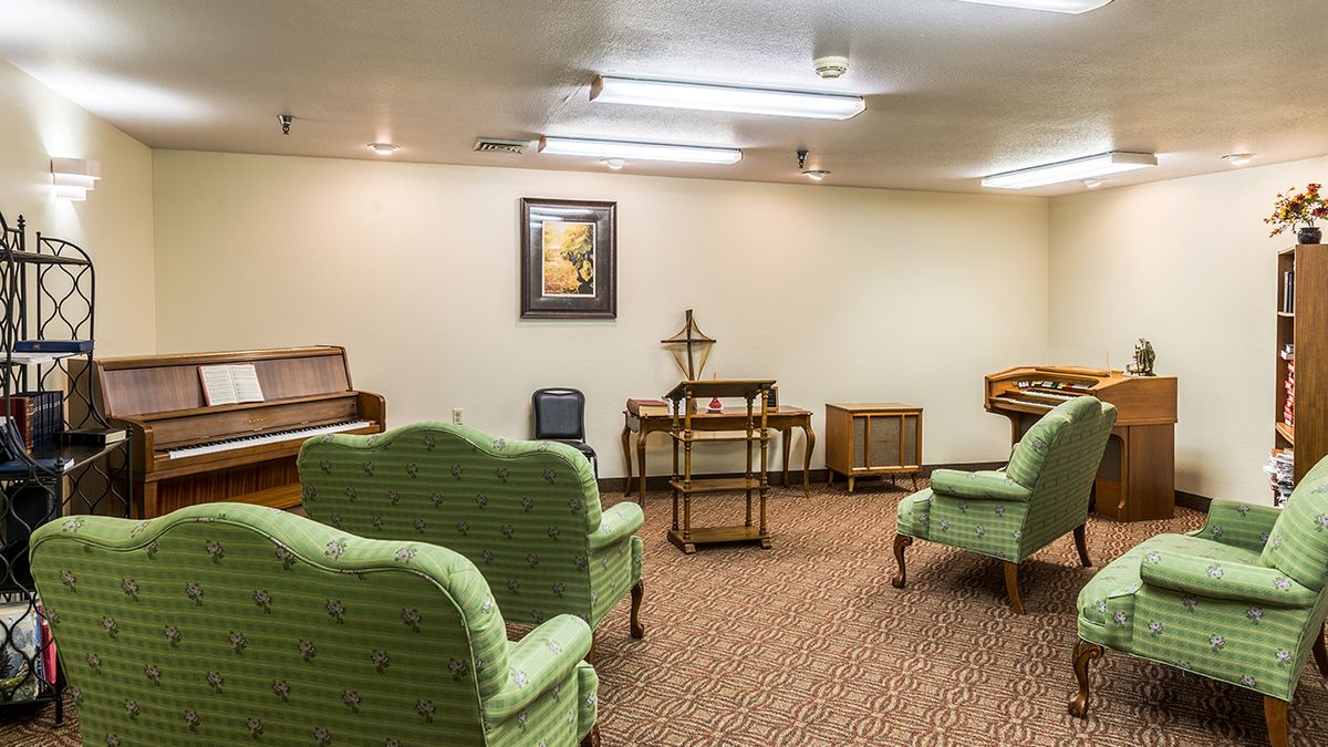 A retro-style room with green chairs, a piano, and vintage furniture on a carpeted floor.
