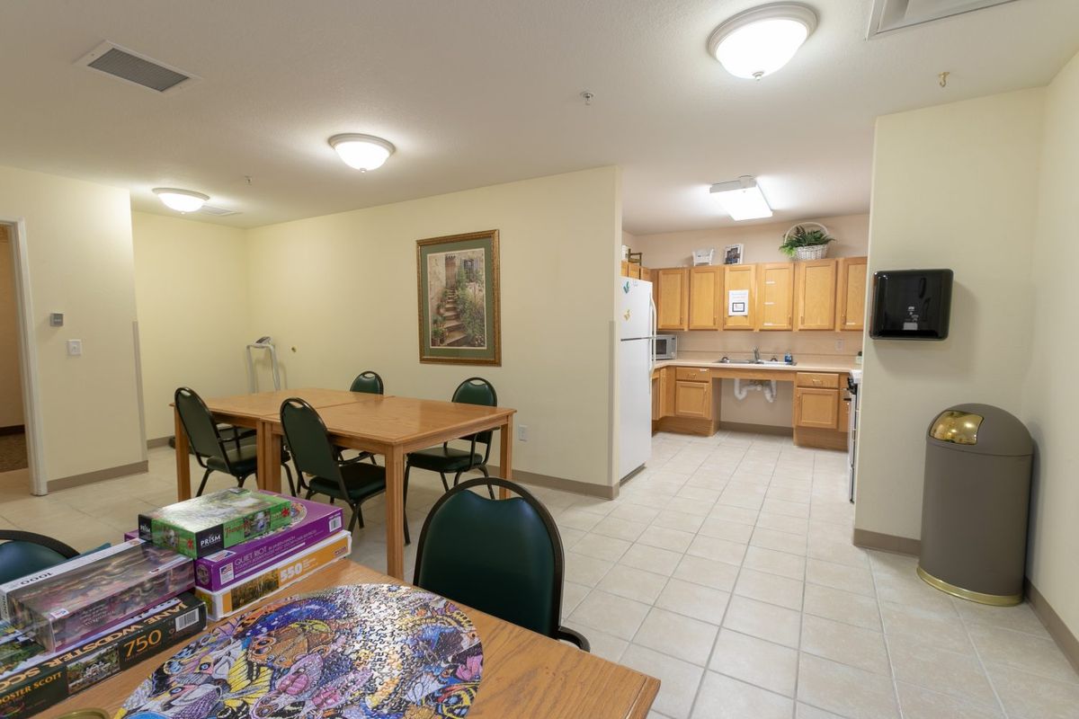A dining area with multiple tables and chairs adjoins a kitchen with wooden cabinetry.