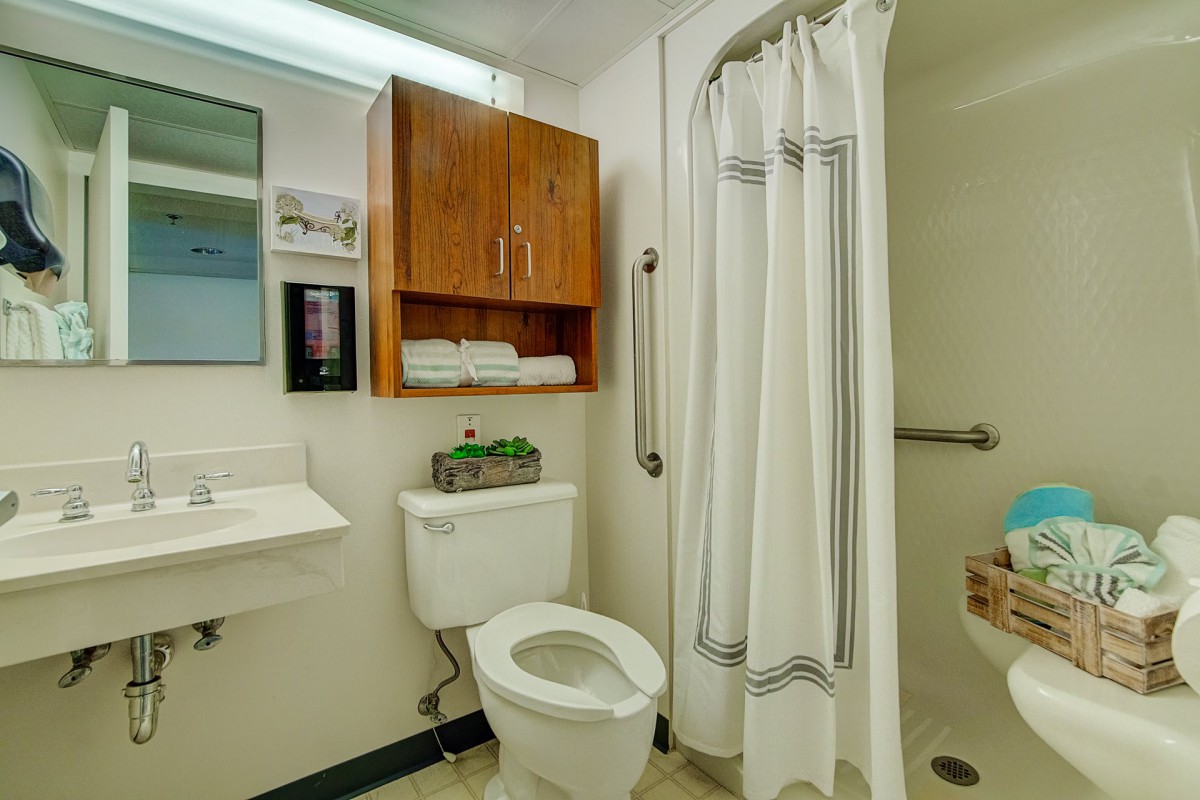 A clean and organized bathroom with a toilet, shower, sink, and storage cabinet.