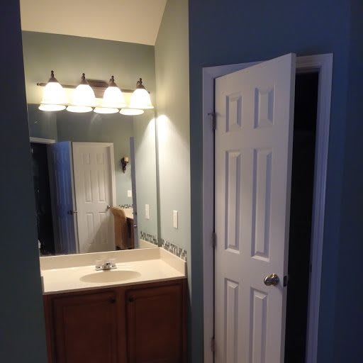 A bathroom with a large mirror, sink, and bright overhead lighting beside an open door.