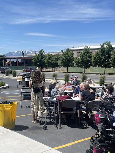 A community gathering outdoors on a sunny day, with people enjoying food at tables against a backdrop of mountains.