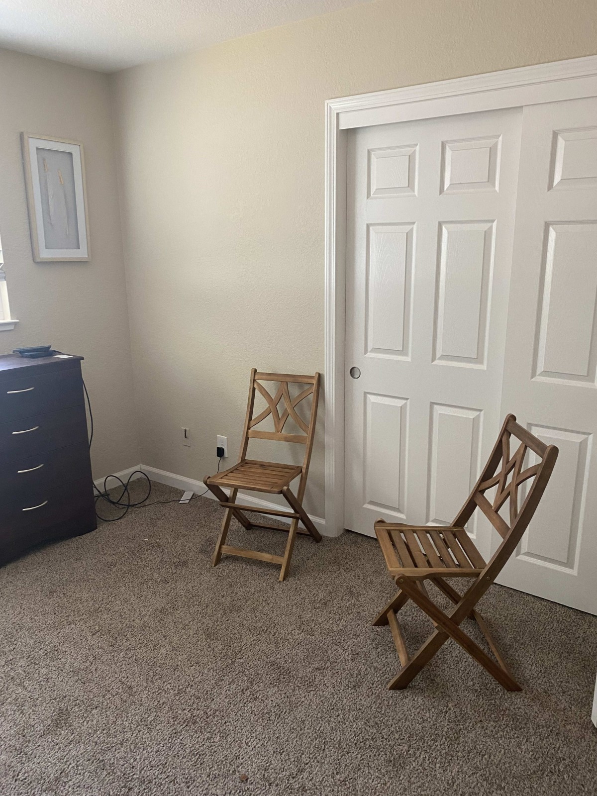A minimalist room with two wooden chairs, a dresser, and a closet.