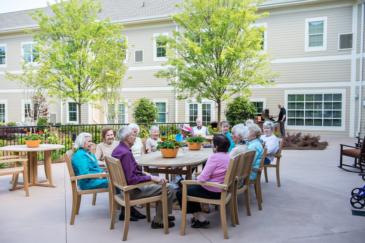 A group of seniors enjoying a gathering outdoors on a sunny day in a retirement community.