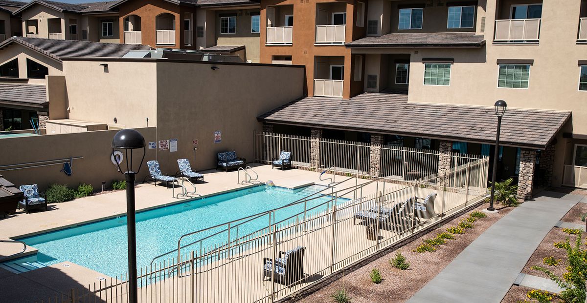 An outdoor swimming pool in an apartment complex with lounge chairs and surrounding fence.