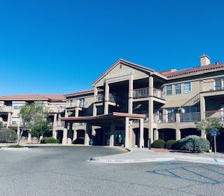 A large residential building complex with a covered entrance under a clear blue sky.
