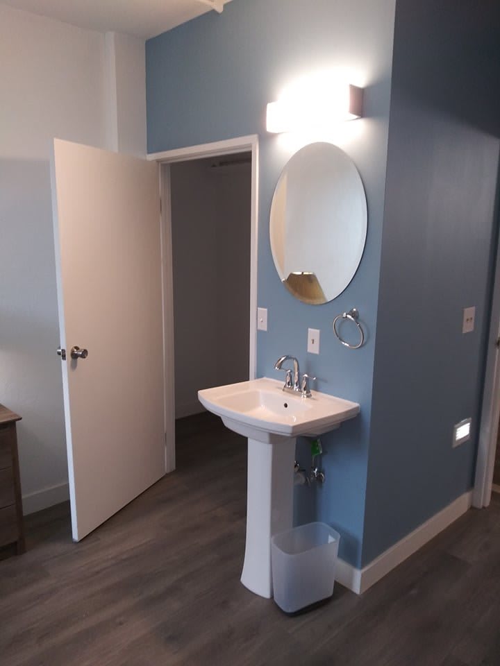 A bathroom with a pedestal sink, circular mirror, and blue walls.