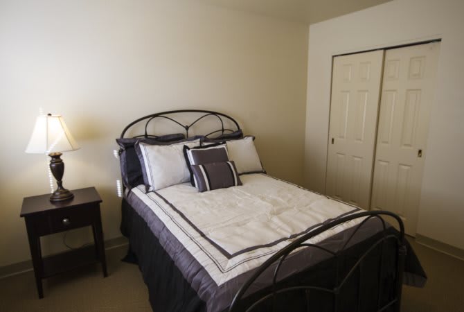 A neatly arranged bedroom featuring a bed with multiple pillows and a bedside lamp.