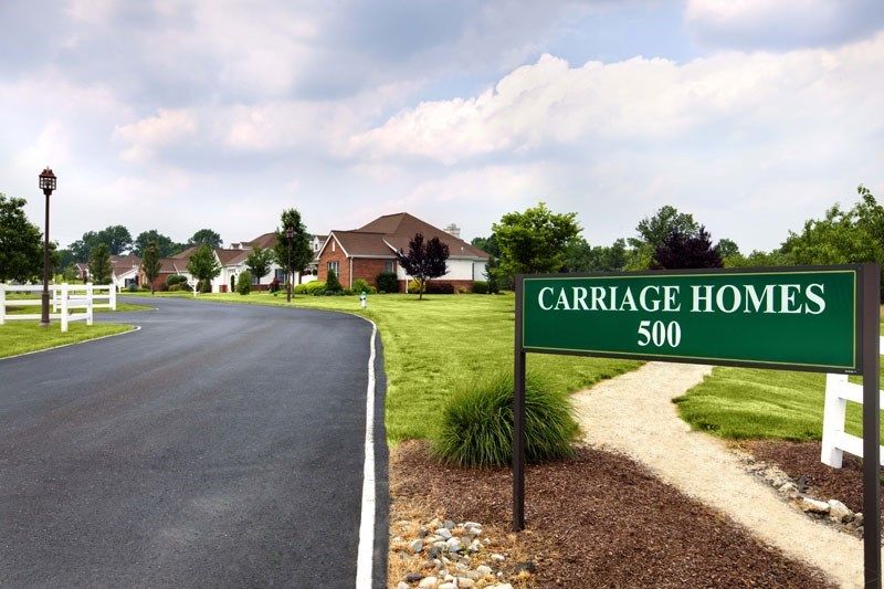 A residential neighborhood with a sign reading 'Carriage Ho 500' along a paved road.