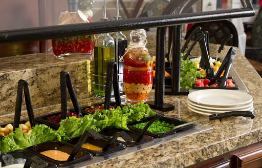 A buffet salad bar featuring fresh vegetables and condiments.
