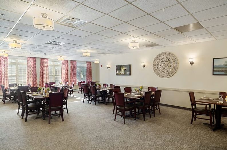 A spacious dining room with arranged tables and chairs, featuring soft lighting and decorative elements.
