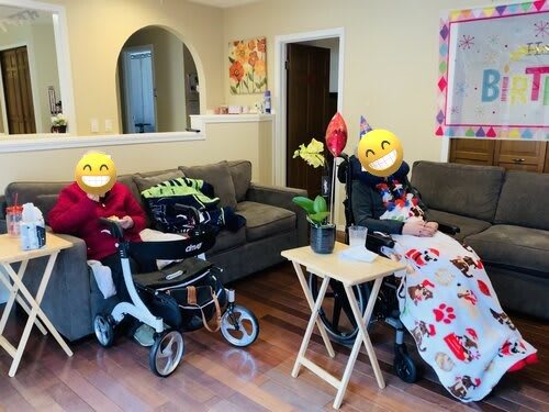 Two people smiling while sitting in wheelchairs in a cozy living room.