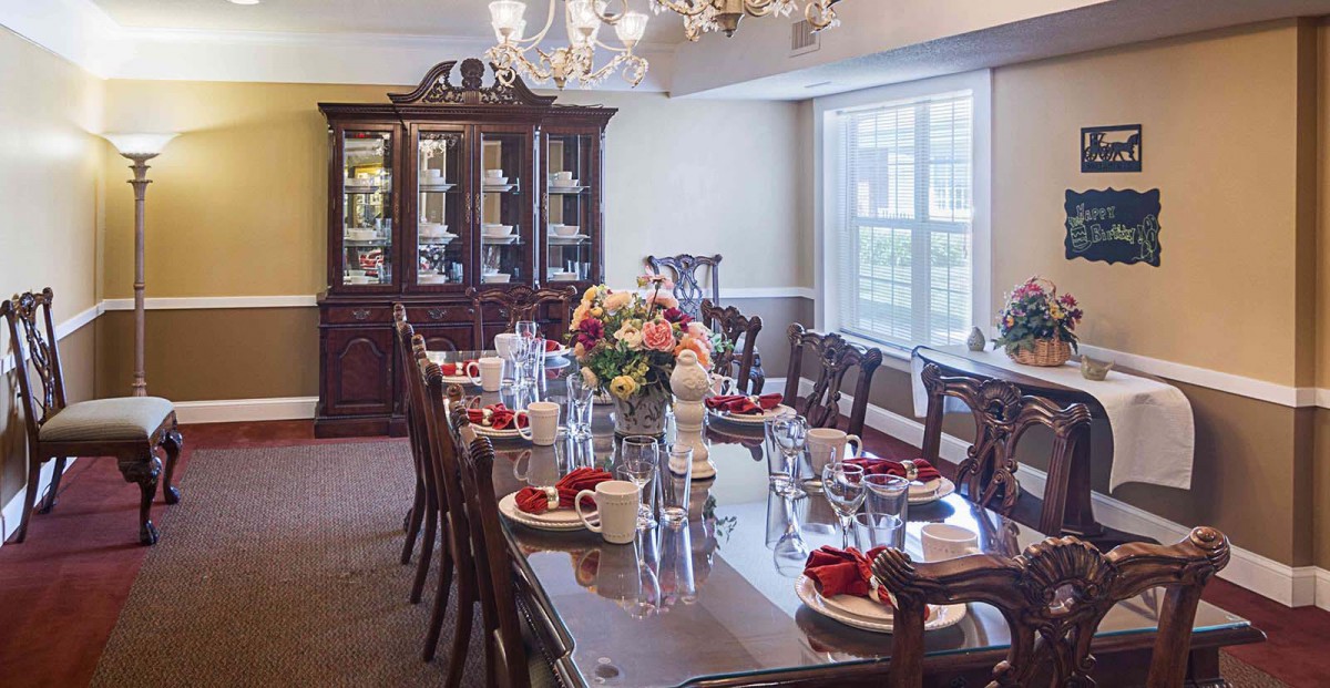 A beautifully set dining room with a long table, elegant chandelier, and a china cabinet in the background.