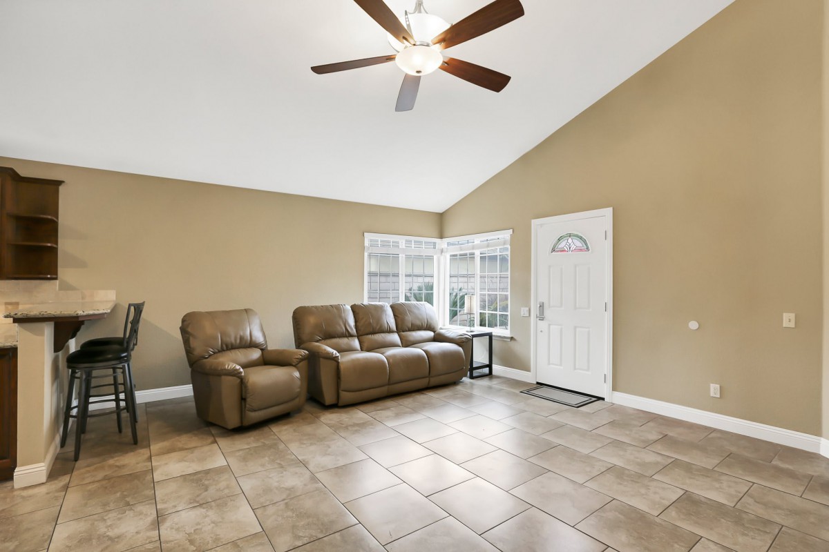 A cozy living room with a brown sofa, ceiling fan, and tiled floor.