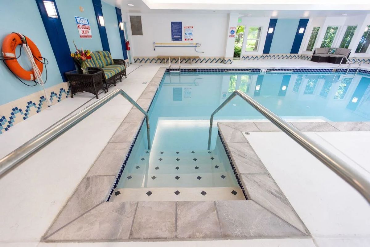 An indoor swimming pool with steps leading into the water, surrounded by a clean, brightly lit area.