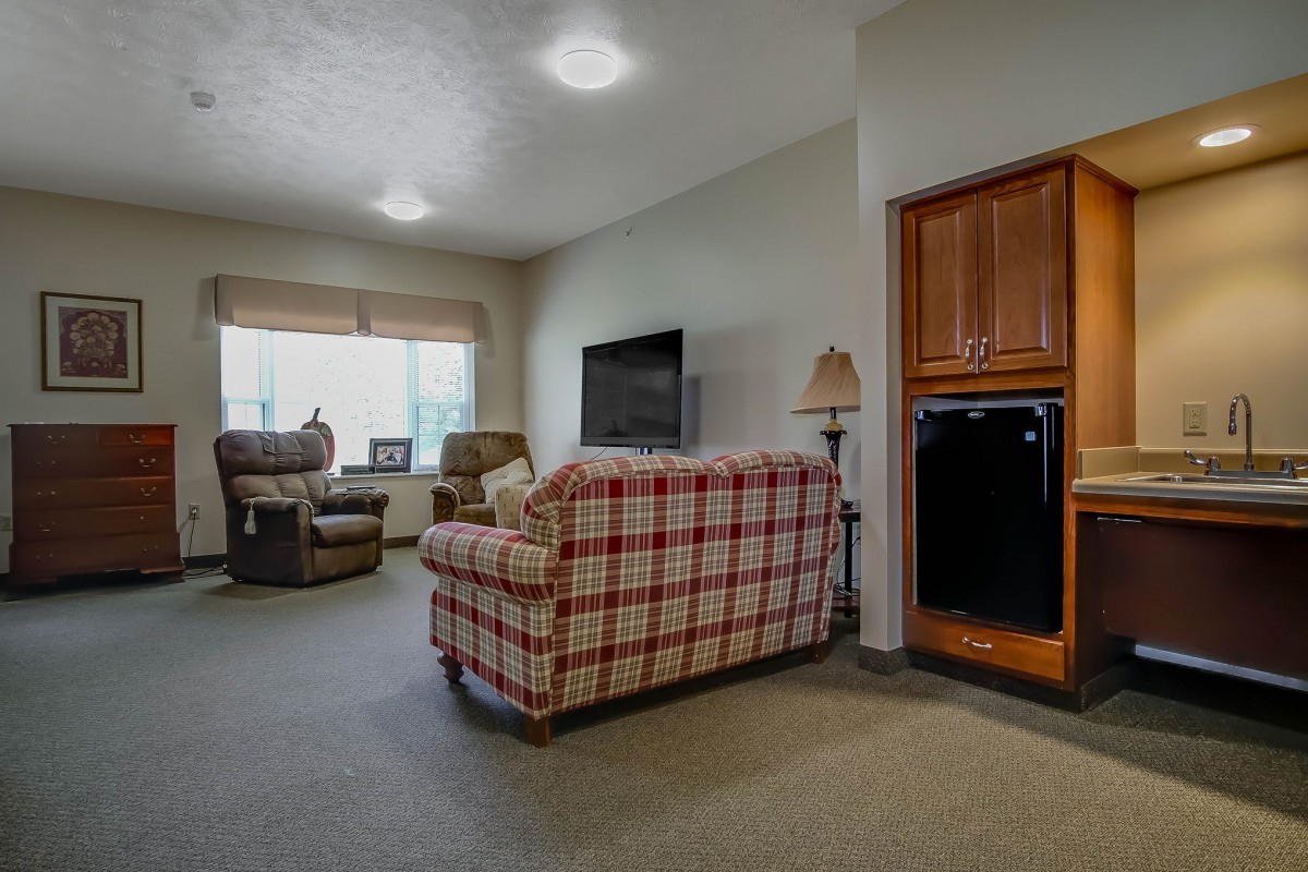 A cozy living room with a plaid sofa, armchairs, and a large television.